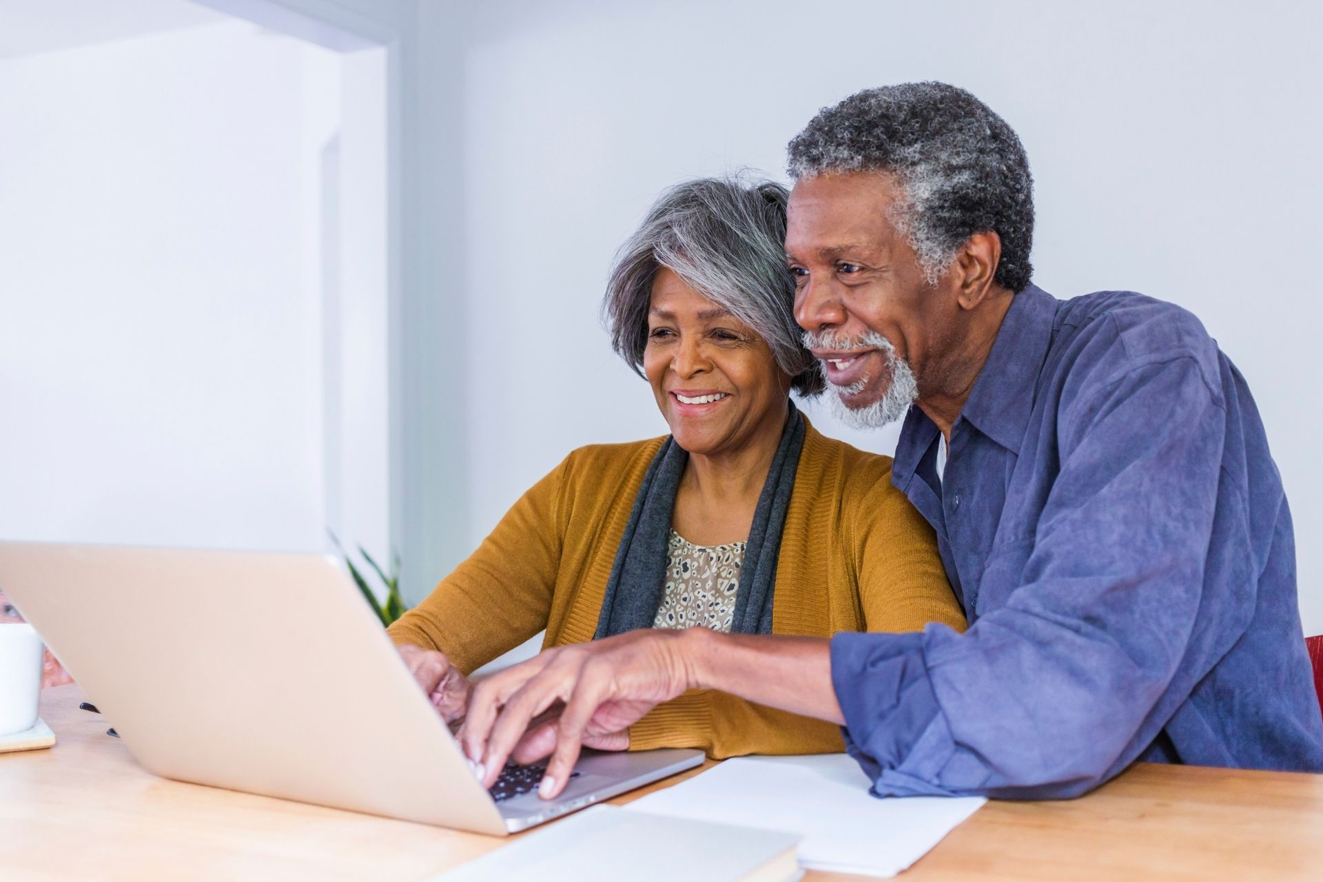 Smiling older Black couple sitting at a table, using a laptop together as they look at the screen
